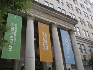 Johns Hopkins Bloomberg School of Public Health building close up view of banner in between columns saying Bloomberg Public Health 100 years and beyond.