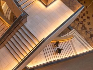 A from-the-ceiling view of two diverging staircases, with two people descending the lower staircase.